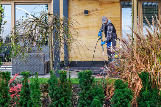 Worker pressure washing a patio beside autumn garden plants