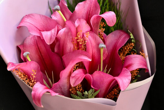 pink lily flower bouquet wrapped in light purple paper tied with satin ribbon, vibrant pink lilies floral arrangement resting on wooden table, elegant gift bouquet close up