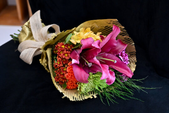 vibrant flower bouquet wrapped in craft paper resting on dark surface, colorful floral arrangement with pink lilies, orange celosia and green chrysanthemum, gift bouquet close up