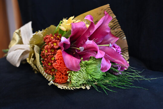 vibrant flower bouquet wrapped in textured kraft paper with burlap ribbon, floral arrangement with large pink lily and purple carnations against wooden background, gift bouquet close up