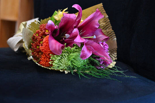 vibrant flower bouquet wrapped in craft paper resting on dark surface, colorful floral arrangement with pink lilies, orange celosia and green chrysanthemum, gift bouquet close up