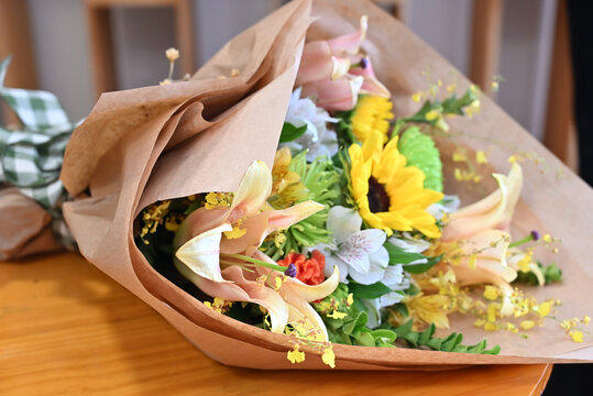 colorful flower bouquet wrapped in kraft paper, vibrant floral arrangement with sunflower, peach lilies, white alstroemeria and yellow orchids, gift bouquet close up