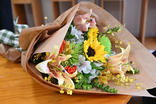 colorful flower bouquet wrapped in kraft paper, vibrant floral arrangement with sunflower, peach lilies, white alstroemeria and yellow orchids, gift bouquet close up