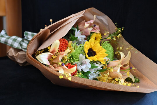 colorful flower bouquet wrapped in kraft paper, vibrant floral arrangement with sunflower, peach lilies, white alstroemeria and yellow orchids, gift bouquet close up