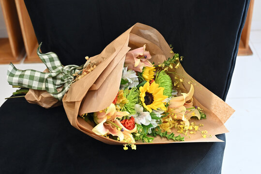 colorful flower bouquet wrapped in kraft paper, vibrant floral arrangement with sunflower, peach lilies, white alstroemeria and yellow orchids, gift bouquet close up