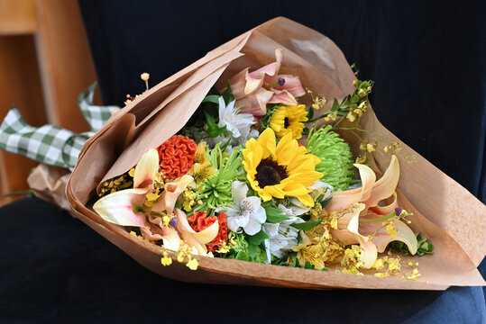 colorful flower bouquet wrapped in kraft paper, vibrant floral arrangement with sunflower, peach lilies, white alstroemeria and yellow orchids, gift bouquet close up