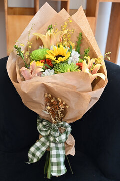 colorful flower bouquet wrapped in kraft paper, vibrant floral arrangement with sunflower, peach lilies, white alstroemeria and yellow orchids, gift bouquet close up