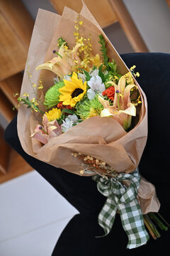 colorful flower bouquet wrapped in kraft paper, vibrant floral arrangement with sunflower, peach lilies, white alstroemeria and yellow orchids, gift bouquet close up