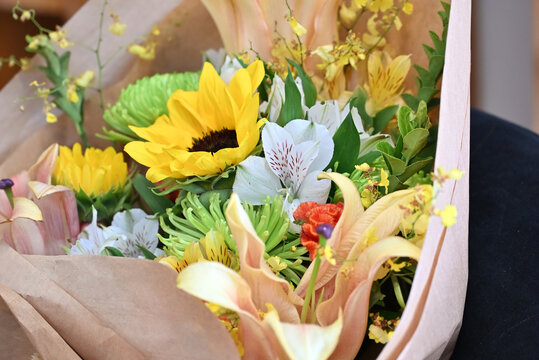 colorful flower bouquet wrapped in kraft paper, vibrant floral arrangement with sunflower, peach lilies, white alstroemeria and yellow orchids, gift bouquet close up