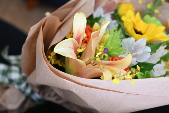 colorful flower bouquet wrapped in kraft paper, vibrant floral arrangement with sunflower, peach lilies, white alstroemeria and yellow orchids, gift bouquet close up