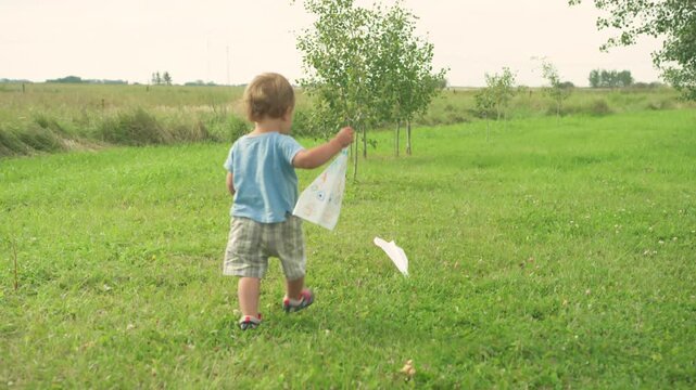 Toddler throwing paper airplane into wide open field from backyard
