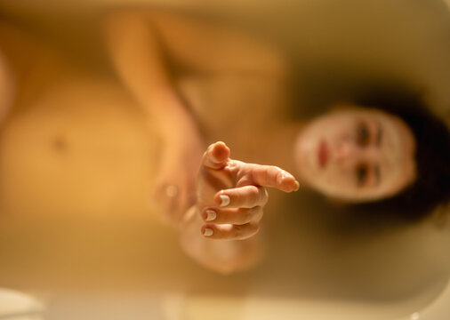 Woman reaching hand out of warm bath water, close-up focused on fingers, cozy aesthetic skin care concept