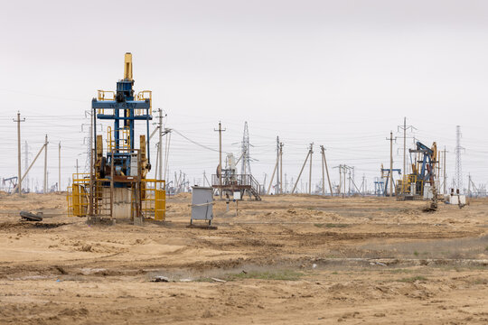View of oil pump jacks operating in an oil field with power lines stretching across the arid desert landscape in Zhanaozen, Mangystau Region, Kazakhstan.