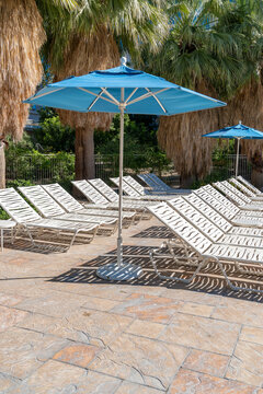 Empty Poolside Chaise Lounge Chairs Under Blue Umbrellas