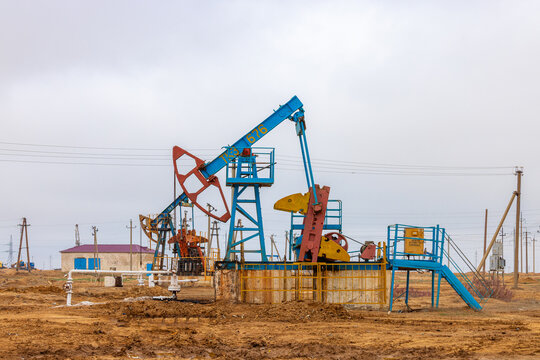 View of an oil pump jack operating in an oil field with industrial machinery and pipelines under a cloudy sky in Zhanaozen, Mangystau Region, Kazakhstan.