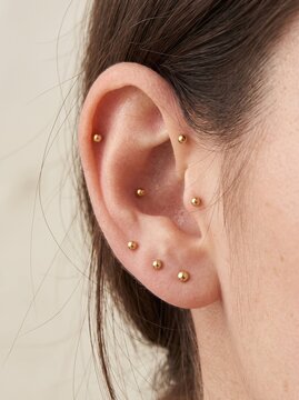 Close up of woman ear with multiple gold stud piercings along cartilage and lobe