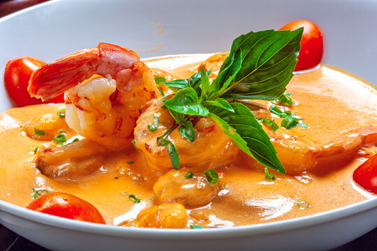 Gourmet large shrimp in a creamy orange sauce, garnished with fresh basil and cherry tomatoes in a white bowl.