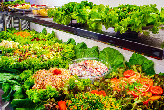Vibrant self-service salad bar featuring a rich variety of fresh greens, sliced tomatoes, mixed vegetables, and fruit salads on a buffet counter.