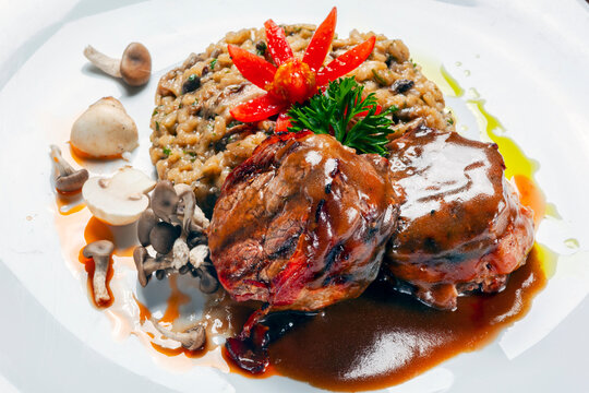 Gourmet plated dish of bacon-wrapped beef medallions, wild mushroom risotto, and rich demi-glace sauce.