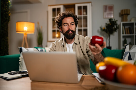 Man learning nutrition online, holding red apple
