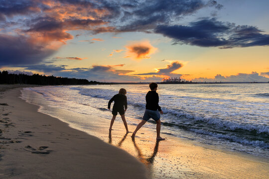 Happy children jump into the water on the beach at sunset. Gdansk, Poland