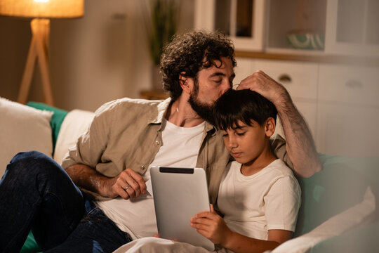 Father kissing son's head while using tablet