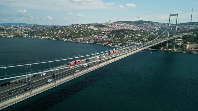 Turkey, Istanbul 01 10 2025: 4K drone video moving backwards along Bosphorus Bridge deck with passing traffic, sailing boats, Grand Camlica Mosque and Camlica Tower on a cloudy day.