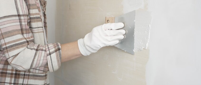 Unknown female construction worker wearing protective gloves applying plaster, smoothing wall surface during home renovation work