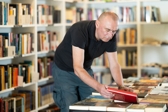 Adult man stands in bookstore, carefully browsing shelves and selecting book of interest