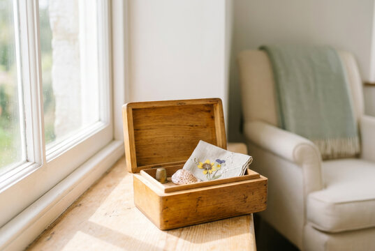 Small reminiscence memory box with simple treasured keepsakes resting on a bright windowsill. Gentle daylight, calm, uncluttered, nostalgia, remembering the past with copy space.
