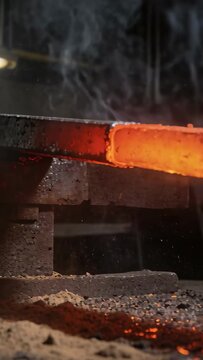 Vertical video: Flaking scale and spraying sparks from hot bar hitting anvil at forge, smoke rising