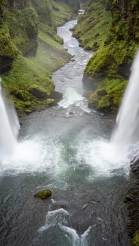 Vertical video: Gorge forcing two falls plunging into pool, sending foam into river, moss cliffs