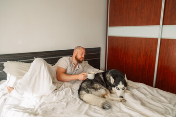 Man with a coffee mug lying beside his sleeping husky © iwavephoto