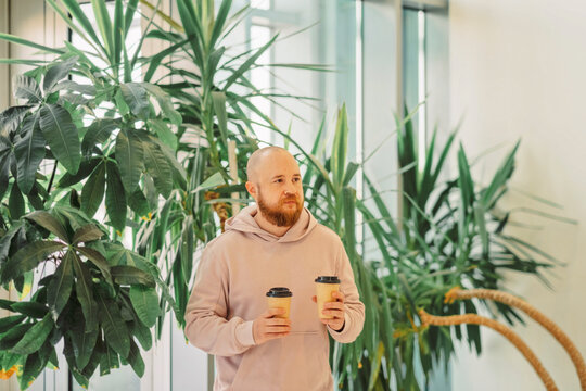Man with a coffee standing among tall indoor plants