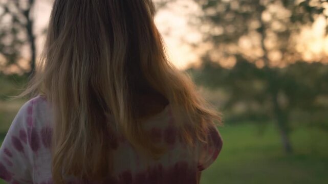 Woman in tie-dye shirt gazing out at garden and field at golden hour