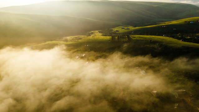 Aerial view of Obudu Mountain Resort nestled among lush green hills and rolling landscapes partially obscured by morning mist during golden hour in Obudu, Cross River, Nigeria.