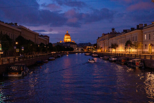 Historic city river canal with cruise boat and illuminated cathedral dome at twilight blue hour.
