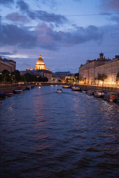 Historic city river canal with cruise boat and illuminated cathedral dome at twilight blue hour.
