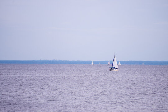 White sailing yacht sailboat floating on calm sea water at sunset evening horizon.
