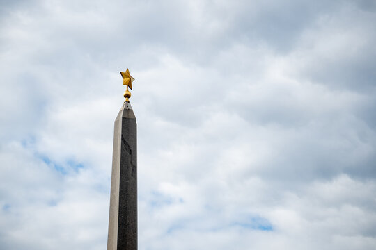Monumental granite stone obelisk tower with golden star on top close up.
