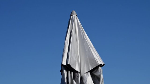A closed white umbrella stands upright against a clear, vibrant blue sky.
