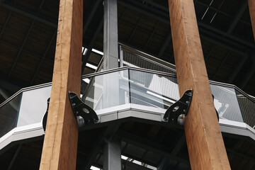 Naklejka premium Modern elevated walkway supported by large wooden columns and steel framework. Glass railings and structural details form contemporary architecture and public building design background.
