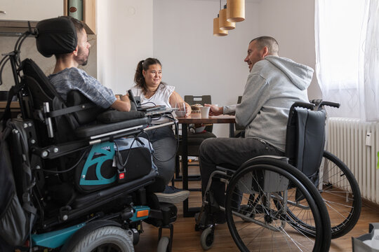Two persons with disabilities and a Personal assistant enjoying talking together and drinking coffee in the home environment.