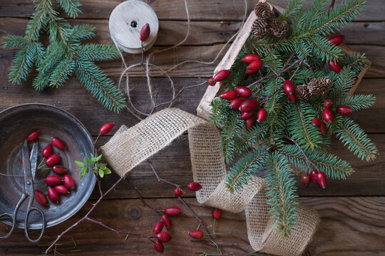 Rustic flatlay of red rosehips and spruce branches with vintage scissors and burlap ribbon for crafting on a wooden table at Christmas