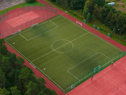 Aerial view of the sports complex in Traku Voke with a football pitch, red running track, and adjacent courts surrounded by forest in Vilnius, Vilniaus apskritis, Lithuania.