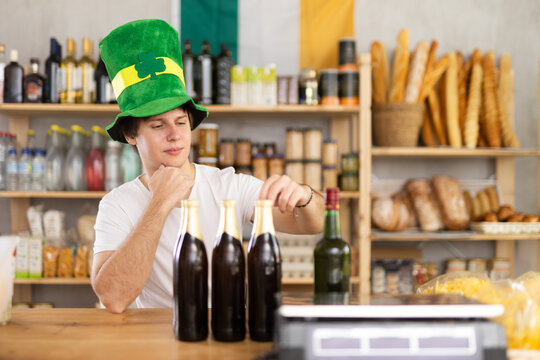 Male employee stand near store counter and waits for visitors in grocery store. On eve of St. Patricks Day, seller wants to sell large amount of alcohol, increase average check