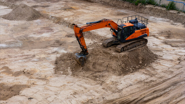 Aerial view of an orange excavator working on a sandy construction site in Gdansk, Poland.