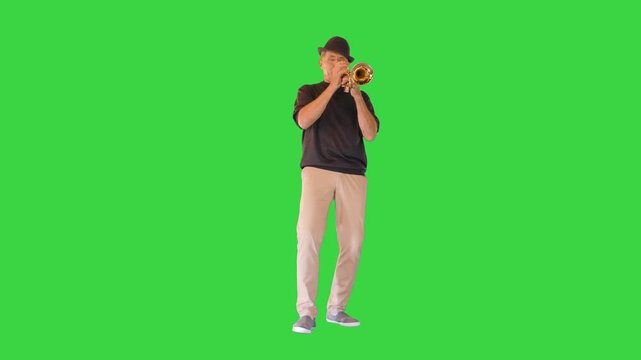 A senior man in black hat plays the trumpet on a Green Screen, Chroma Key.