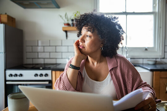 Middle aged woman reviewing bills at home kitchen table