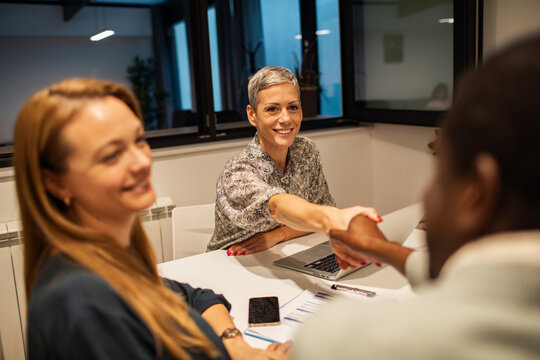 Smiling hiring managers shake hands with candidate in office